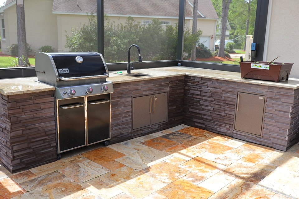 An outdoor kitchen underneath a covered patio complete with grill, sink and cabinets